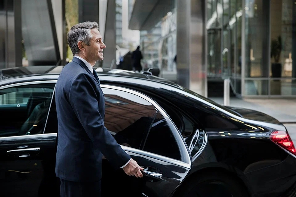 Chauffeur opening the rear passenger door of a black sedan