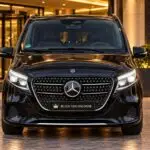 Black Mercedes-Benz V-Class chauffeur van, front view at a hotel-style entrance