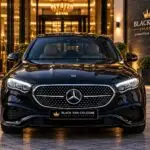 Black Mercedes-Benz E-Class chauffeur sedan, front exterior view with illuminated headlights